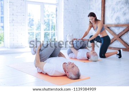 Wait a second. Grey-haired woman lying on the orange mat and talking to her tutor while holding legs together