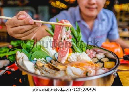 enjoy eating Shabu Shabu and Sukiyaki in hot pot at japanese restaurant.Japanese food are high quality food cooking in hot boil soup with vegetable beef raw meat or seafood hold with chopsticksshabu Royalty-Free Stock Photo #1139398406