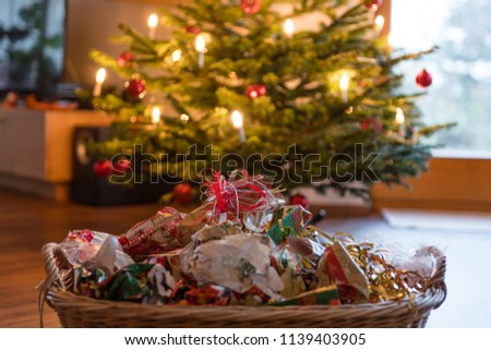 Packaging waste in a basket in front of the decorated chrismas tree Royalty-Free Stock Photo #1139403905