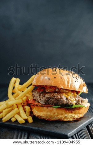homemade  juicy burger on dark wooden board with French fries. Street food, fast food.