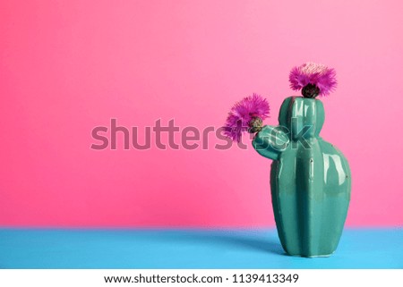Trendy cactus shaped ceramic vase with flowers on table against color background