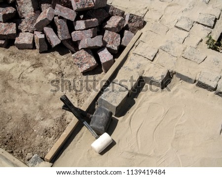 Two rubber Mallets among a pile of granite stones for paving. In the process of paving granite stones - unfinished work, top view