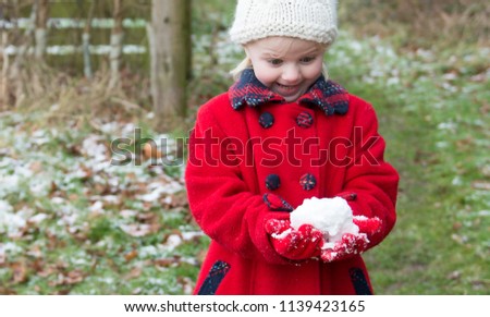  A little girl in a red coat plays amazed with a snowball on a snowy day in the mountains at Christmas time, funny snow picture