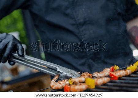 chef in black uniforms and gloves fries shrimp and vegetables on the BBQ