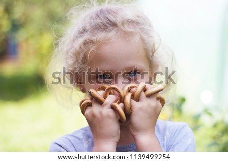 A funny portrait of an adorable blue-eyed little girl with fluffy curly blonde hair with the bagels on her fingers Royalty-Free Stock Photo #1139499254