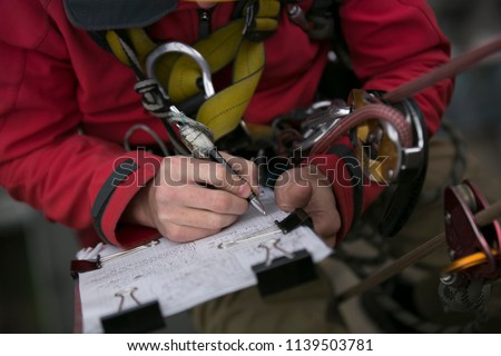 Close up picture of rope access technician engineer worker writing a report of building structure leak, hiatus at hight rise construction building site Sydney, city skyline, Australia      
