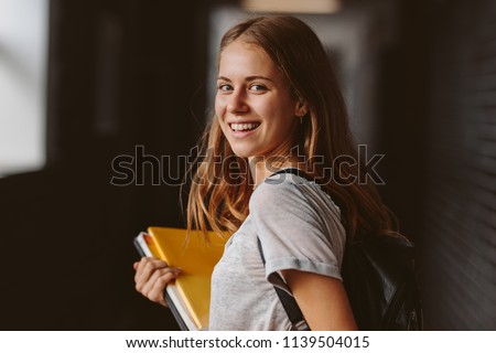 Rear view of beautiful girl walking through university hallway looking back and smiling. female student going for the lecture. Royalty-Free Stock Photo #1139504015