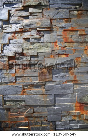 Close up outdoor view of part of a stone bricks wall with several rusty shapes. Pattern of grey geometric blocks. Graphic image with various polygons, angles and lines. Abstract architectural picture.