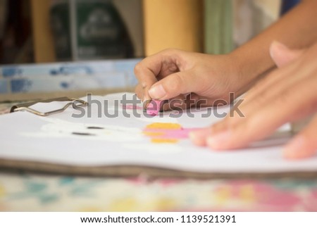 Children's hands are drawing and coloring on white paper.