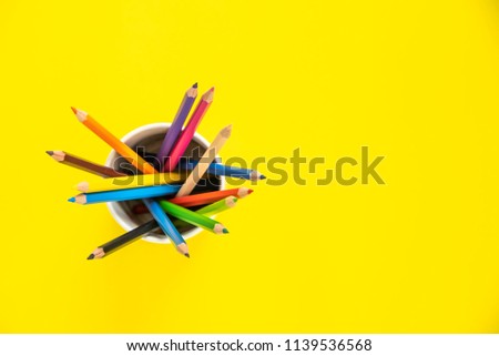 Stack of colored pencils in a glass on yellow background