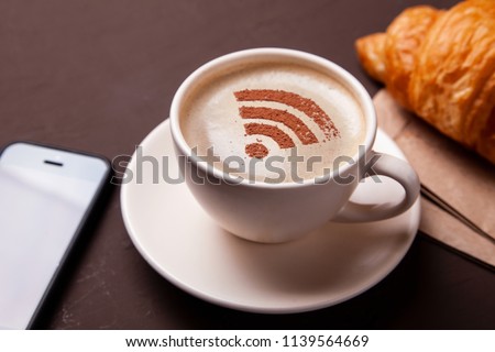 Cup of coffee with WiFi sign on the foam. Free access point to the Internet WiFi. I like coffee break with croissant