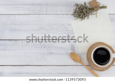 Blank white card and a cup of coffee with caspia bouquet on white wood background with copy space