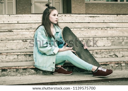 On the old steps a young girl with a skateboard. Modern youth, a new generation. Blue denim jacket and pants, sneakers. Look into the distance. Muted tone, vignetting.