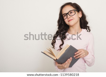 Education and school concept. Little girl in glasses reading book, copy space
