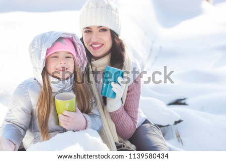 Mother and her daughter having fun outdoors in winter time. Pretty family drinking tea and cocoa