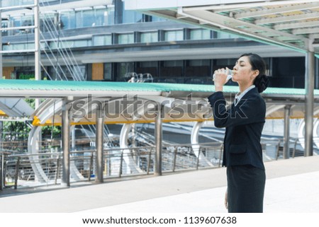 Asian businesswoman standing and drinking pure mineral water from plastic bottle in the city.