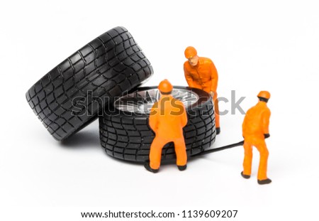 The concept of the workshop tire fitting. Miniature mechanics repairing dusty toy car wheel, close up.