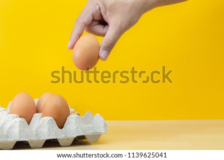 hand picked fresh egg from paper tray, on wood table and yellow background