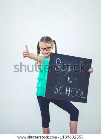 girl with glasses is holding blackboard with the words back to school on it