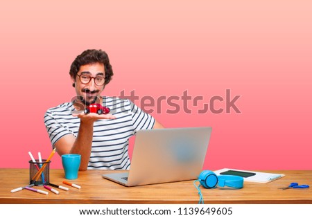 young crazy graphic designer on a desk with a laptop and with a red car model