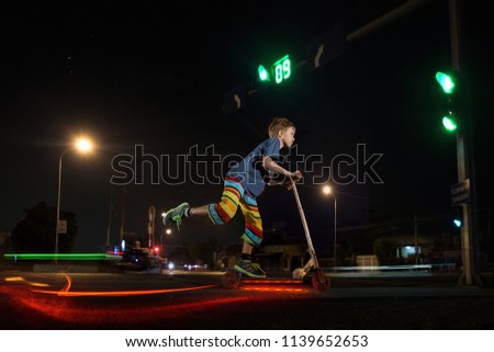 A young kid riding scooter with light at night