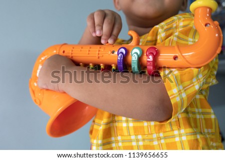 small child holding and playing with plastic saxophone toy in arms