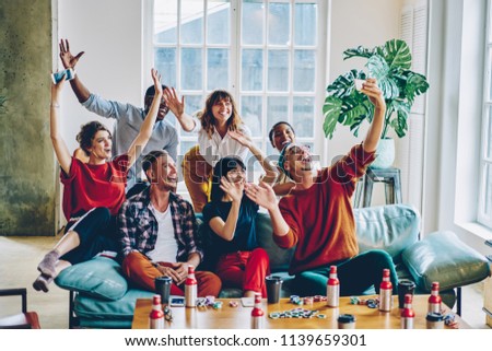Happy multicultural hipster guys dressed in casual wear holding hands up and smiling a camera of modern smartphone making selfie photo.Positive young people spending time together and taking picture