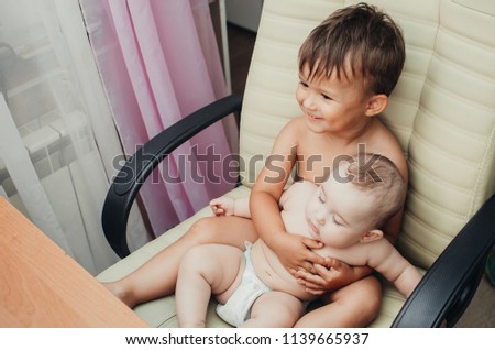 Brother and younger sister sitting on a chair and hugs her
