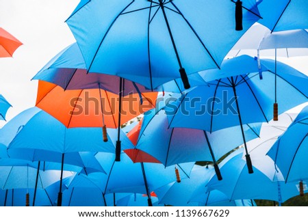 Colored umbrellas hang in the air as a protective roof against rain and sunshine. They form a colorful tile pattern.