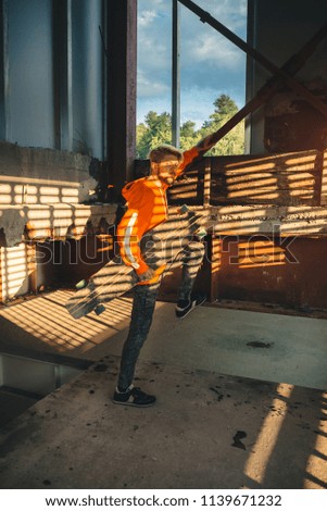 Hipster man with skateboard in abandoned building going to run through the window. Image with grain