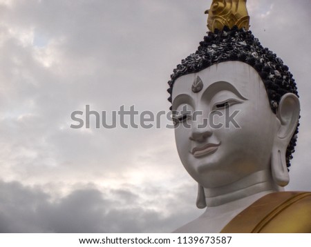 Photographs only of the head of a large statue of the Buddha and the sky is covered with clouds.