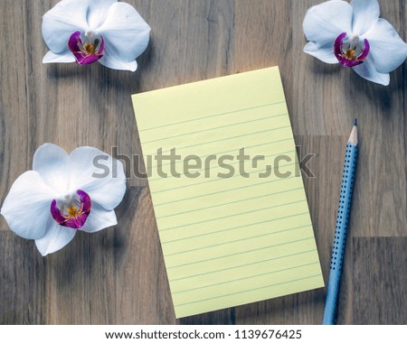 Leaf pad for writing. Background for inspiration. Notepad page and white orchids on a wooden table top.