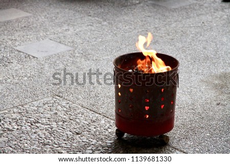Burning paper money with orange flame in the red steel tub. The traditional religious ceremony of Taoism in Taiwan.