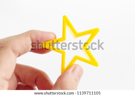Human hand holding a small yellow plastic mold in star shape over a white background implying score rating or admiration.