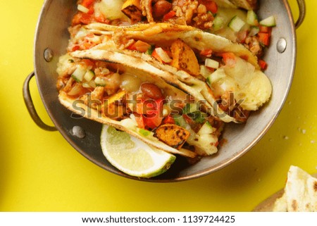 Close up of mexican tacos with chili con carnes and grated cheese served over a yellow background