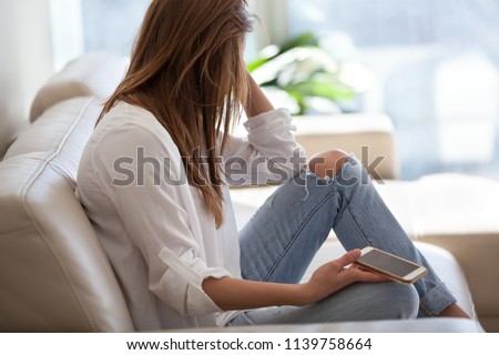Jealous woman sitting on sofa holding phone feeling sad waiting for call, frustrated millennial girl upset or worried receiving bad news in mobile message on smartphone at home, cyberbullying concept Royalty-Free Stock Photo #1139758664