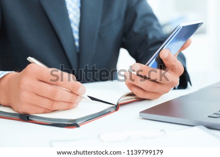 Businessman in black suit using mobile smart phone and working on laptop computer close up. Just hands handss over the table.