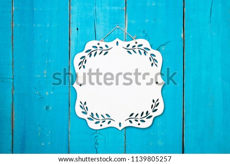 Blank wood sign with floral border hanging on antique rustic teal blue wooden door; message board with copy space