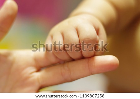 Baby holding finger of his mother giving senses of attachment and bonding. The image taken with a selective focus stressing an emotional scene. Royalty-Free Stock Photo #1139807258