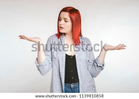 Red haired plus size ordinary woman standing on a neutral grey background. Emotional portrait. She dont know what to choose