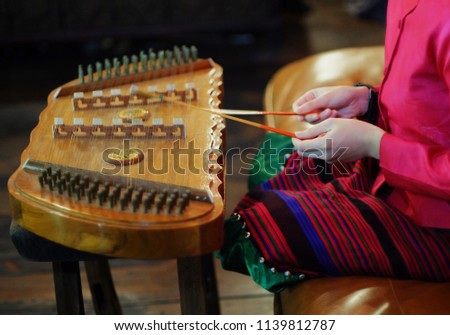 a girl in thai national dress playing dulcimer in blurred room on blurred background
