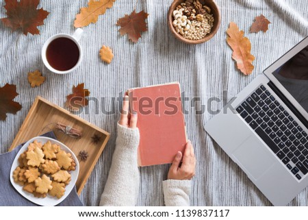Hello Autumn flat lay background. Top view of workspace or office desk on knitted blanket with laptop, tea or coffee cup, maple leaves, vintage book and honey biscuits and cookies.