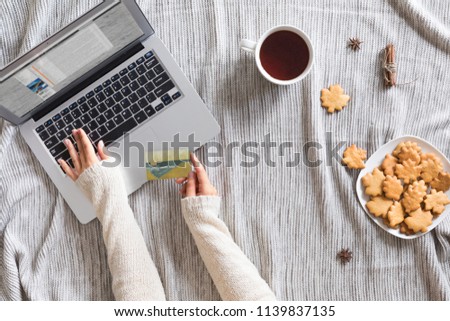Top view of woman hands holding credit card on autumn baclground, business concept, online shopping, workspace with laptop, mobile phone, autumn leaves and flowers and notebook, cookies, flat lay.