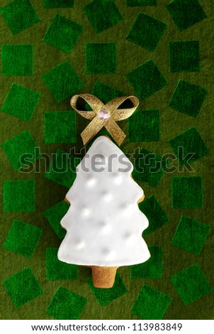 Christmas fir tree background. Ginger and Honey cookie with white sugar decoration and gold bow on the green paper background.