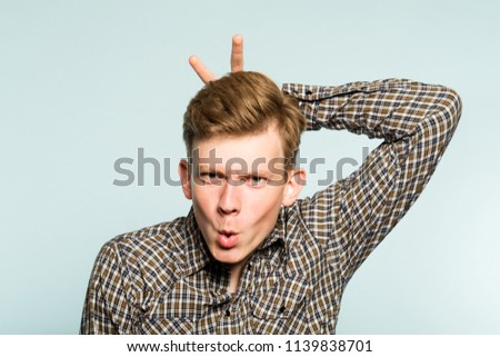 funny joyous happy frolic playful man fooling around giving bunny ears. portrait of a young guy on light background. emotion facial expression. feelings and people reaction.