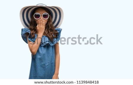 Brunette hispanic girl wearing sunglasses and summer hat cover mouth with hand shocked with shame for mistake, expression of fear, scared in silence, secret concept