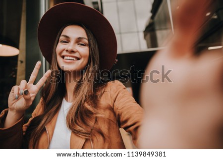 Beautiful woman in brown hat is looking on camera and smiling. She is posing on it. Girl is showing the piece symbol with hands