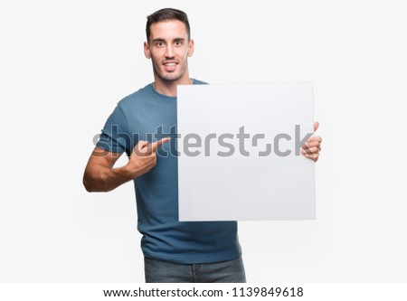 Handsome young man holding advertising banner very happy pointing with hand and finger