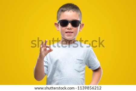 Dark haired little child wearing sunglasses doing ok sign with fingers, excellent symbol