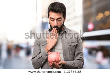 Surprised Handsome man with beard holding a piggybank at outdoor